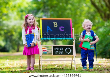 Children happy to be back to school. Preschooler girl and boy with backpack and books at black chalk board learning to write letters and read. Kids at preschool or kindergarten learn the alphabet.