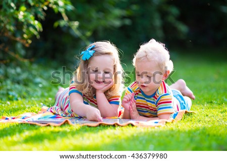 Kids reading a book in summer garden. Children study. Boy and girl play in school yard. Preschool friends playing and learning. Siblings doing homework. Kindergarten kid and toddler read books.