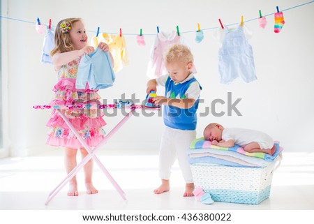 Newborn child on pile of clean dry towels. Brother and sister playing with little sibling. Siblings bonding. Children ironing clothes. Twin kids play with baby boy. New born kid after bath in a towel