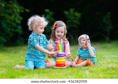 Three little children play with colorful rainbow pyramid toy. Educational toys for young child. Sibling kids building tower together. Toddler boy, preschooler girl and baby build blocks outdoors.