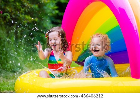 Children playing in inflatable baby pool. Kids swim and splash in colorful garden play center. Happy boy and girl playing with water toys on hot summer day. Family having fun outdoors in the backyard.