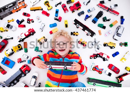 Funny curly toddler boy playing with his model car collection lying on the floor. Transportation and rescue toys for children. Toy mess in kids room. View from above. Many cars for little boys.