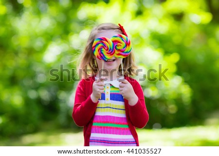 Cute little girl with big colorful lollipop. Child eating sweet candy bar. Sweets for young kids. Summer outdoor fun. Preschooler kid with sugar lolly. Children having snack in a park after preschool.