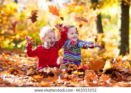 Happy children playing in beautiful autumn park on warm sunny fall day. Kids play with golden maple leaves. Focus on girl.