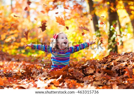 Happy little girl playing in beautiful autumn park on warm sunny fall day. Kids play with golden maple leaves.