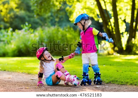 Girl and boy learn to roller skate in summer park. Children wearing protection pads and safety helmet for safe roller skating ride. Active outdoor sport for kids. Siblings help and support each other