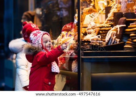 Children window shopping on traditional Christmas market in Germany on snowy winter day. Kids buying candy, pastry and gingerbread in confectionery. Boy and girl choosing sweets in Xmas bakery.