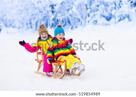 Little girl and boy enjoying sleigh ride. Child sledding. Toddler kid riding a sledge. Children play outdoors in snow. Kids sled in snowy park in winter. Outdoor fun for family Christmas vacation.