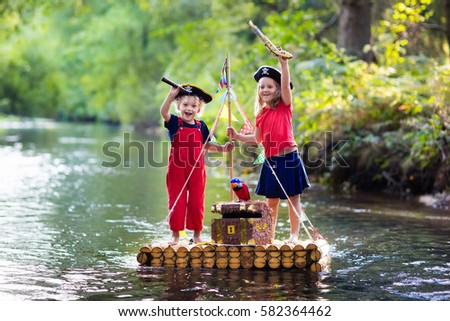 Kids dressed in pirate costumes and hats with treasure chest, spyglasses, and swords playing on wooden raft sailing in a river on hot summer day. Pirates role game for children. Water fun for family
