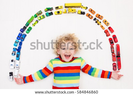 Funny curly toddler boy playing with his model car collection on the floor. Transportation and rescue toys for children. Rainbow toy mess in kids room. View from above. Many cars for little boys.
