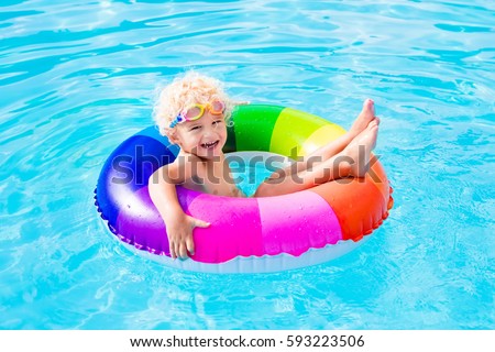Happy little boy playing with colorful inflatable ring in outdoor swimming pool on hot summer day. Kids learn to swim. Child water toys. Children play in tropical resort. Family beach vacation.