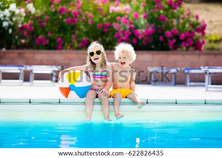 Kids playing at outdoor swimming pool. Little girl and boy play and swim in resort pool on tropical beach island summer family vacation. Swim and eye wear, sun protection, water toys for children.