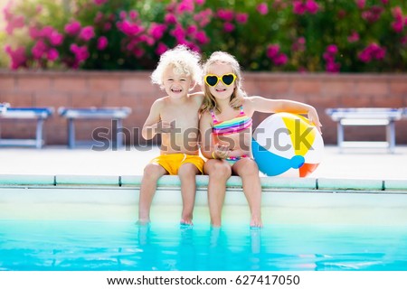 Kids playing at outdoor swimming pool. Little girl and boy play and swim in resort pool on tropical beach island summer family vacation. Swim and eye wear, sun protection, water toys for children
