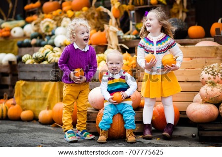 Group of little children enjoying harvest festival celebration at pumpkin patch. Kids picking and carving pumpkins at country farm on warm autumn day. Halloween and Thanksgiving time fun for family.