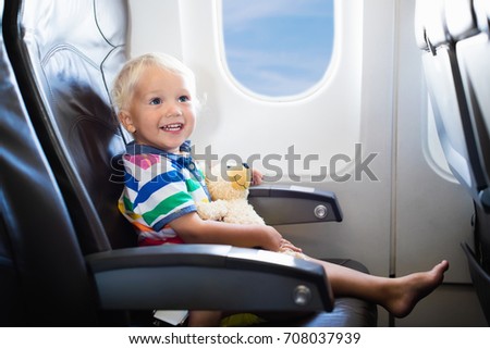 Child in airplane. Kid in air plane sitting in window seat. Flight entertainment for kids. Traveling with young children. Kids fly and travel. Family summer vacation. Baby boy with toy in airplane.