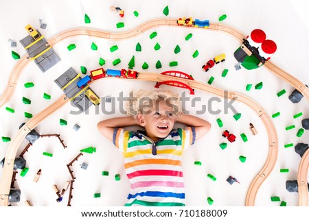Kids play with toy train railway. Child playing with wooden trains. Toys for little boy. Preschooler building rail road and blocks at home or daycare, preschool. Kindergarten educational games.