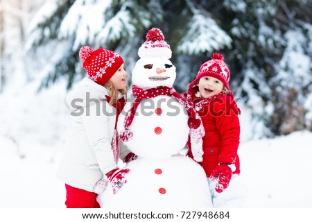 Children build snowman. Kids building snow man playing outdoors on sunny snowy winter day. Outdoor family fun on Christmas vacation. Boy and girl play snow balls. Winter clothing for baby and toddler.
