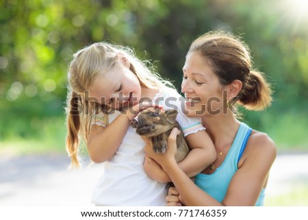 Kids play with farm animals. Child feeding domestic animal. Young mother and little girl holding wild boar baby at petting zoo. Kid playing with newborn pig. Children and pets Family at farm vacation.