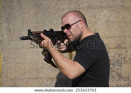 Man with glasses is holding Kalashnikov rifle.
