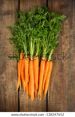 Bunch of fresh carrots with green leaves over wooden background. Vegetable. Nutrition. Raw food ingredients