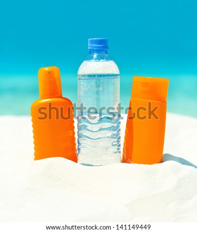 drink water and sun protection cream on sand beach background. skin care concept