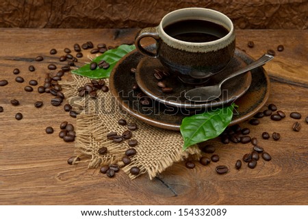 Cup of black coffee with beans and green leaves on wooden background