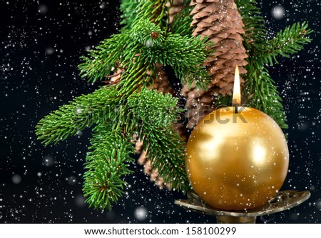 christmas tree branch with golden burning candle over black background with snowfall effect