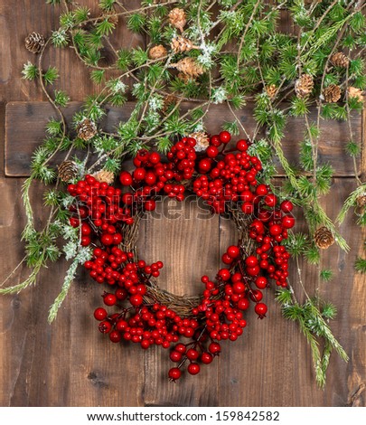green christmas tree branches and wreath from red berries over rustic wooden background. bright festive decoration