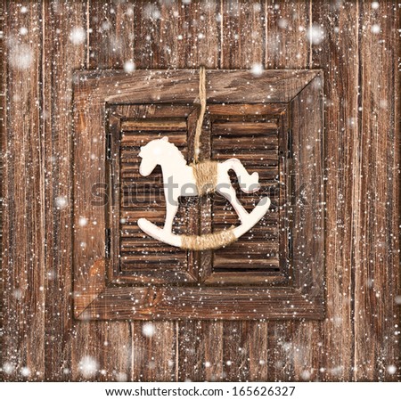 christmas decoration rocking horse over wooden window background. vintage style picture with falling snow effect