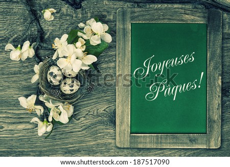 chalkboard, flowers and easter nest with eggs on rustic wooden background with sample text Happy Easter in french. retro style toned picture