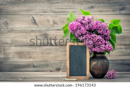 lilac flowers in vase on wooden background. blackboard with space for your text. retro style toned picture