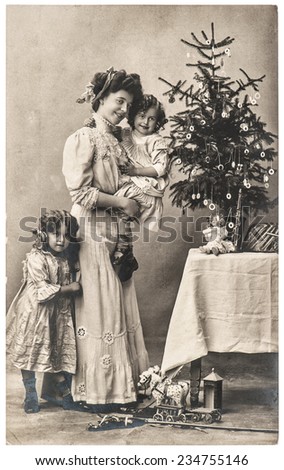 happy mother and children with christmas tree and antique toys. vintage sepia picture with original film grain and blur