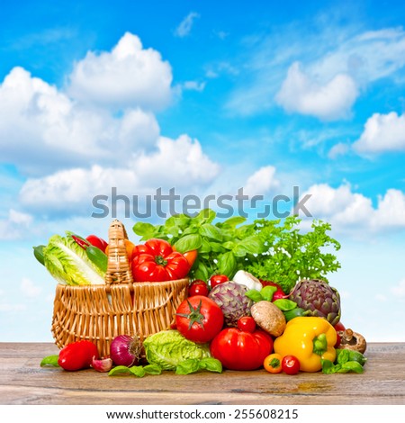 Fresh vegetables and herbs on wooden background over beautiful blue sky. Shopping basket with organic food ingredients