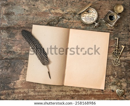 Open book and vintage writing accessories. Feather pen and inkwell on wooden background