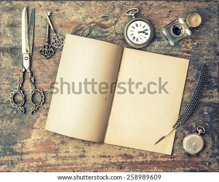 Open journal book and vintage writing tools on wooden table. Feather pen, inkwell, keys on textured background. Retro style toned picture