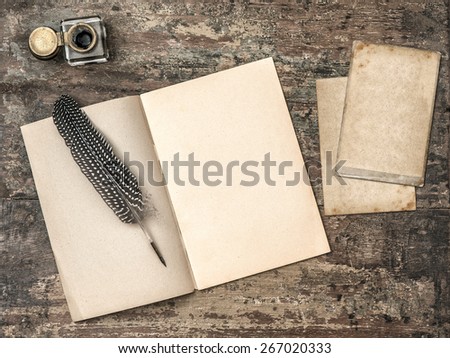 Open book, vintage writing tools feather pen and inkwell on textured wooden background. Retro style toned picture