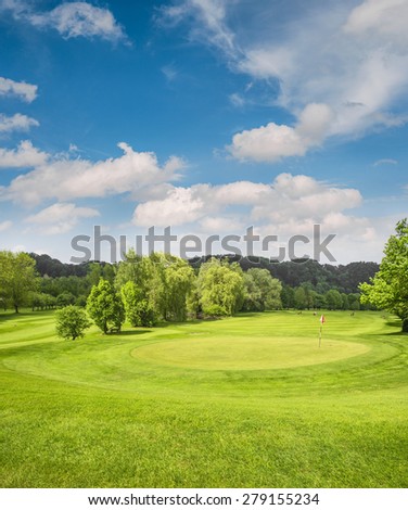 Golf course landscape. Spring field with green grass, trees and cloudy blue sky