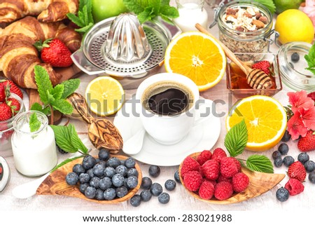 Breakfast coffee, croissants, muesli, honey, granola, fresh berries, fruits orange, apple, milk. Healthy food concept