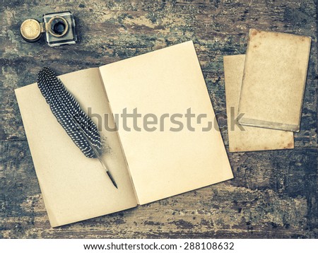 Open book, antique writing tools feather pen and inkwell on textured wooden background. Vintage style toned picture