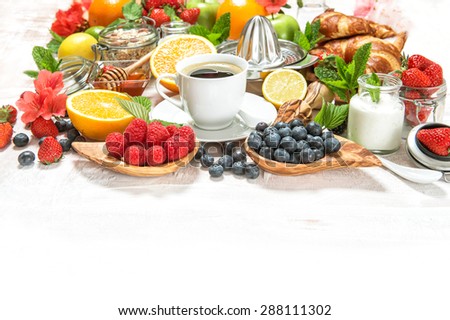 Healthy breakfast table with coffee, croissants, muesli, fresh berries, fruits orange, apple, yogurt, honey, milk. Organic food concept