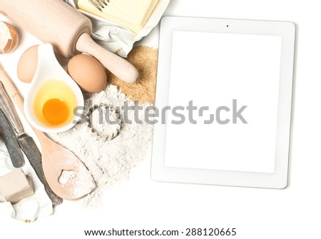 Notebook digital tablet pc and baking ingredients eggs, flour, sugar, butter, yeast. Empty display for your recipe text