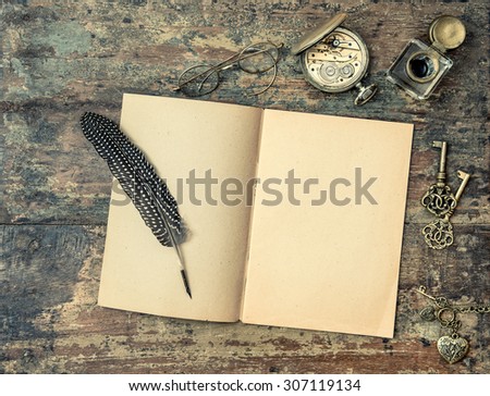 Open book and vintage writing accessories. Feather pen and inkwell on wooden background. Retro style toned picture