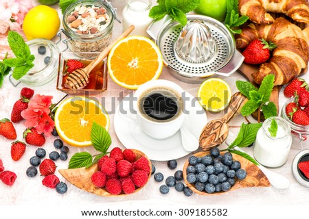 Breakfast with coffee, croissants, granola, honey, fresh berries, fruits orange, apple, milk. Healthy food concept. Selective focus