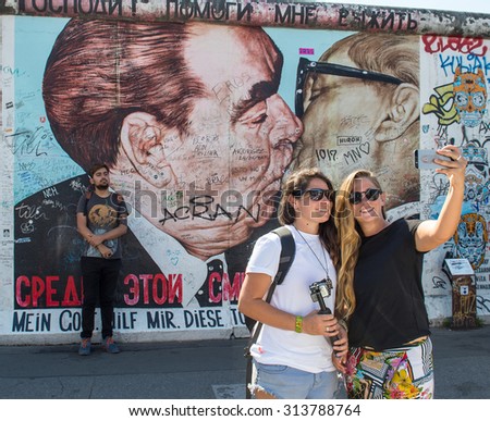 BERLIN, GERMANY - AUGUST 30, 2015: Young people taking selfie pictures on the famous Berlin Wall. Graffiti at the East Side Gallery in Berlin, Germany