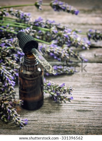 Perfumed herbal oil essence and lavender flowers over rustic wooden background. Vintage toned picture