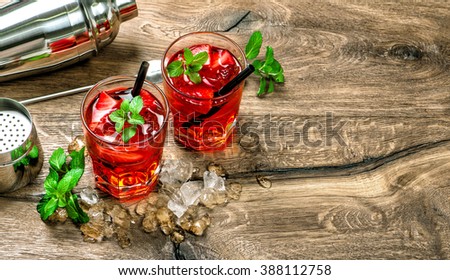 Red cocktail with ice, mint leaves and strawberry on wooden background