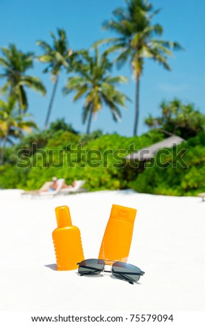 sun protection cream and sunglasses on palm beach. holiday background