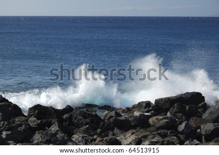 Breaking surf on lava rock shore throws spray into the air on the coast of the Big Island Hawaii
