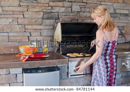 Attractive blond Caucasian woman using a gas barbeque grill in an outdoor kitchen