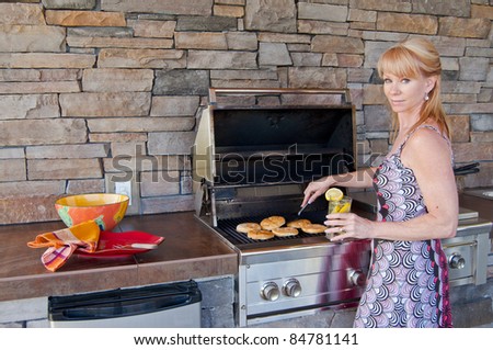 Attractive blond Caucasian woman using a gas barbeque grill in an outdoor kitchen